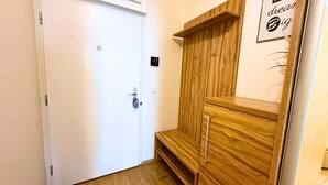 A white door with a keyhole, a wooden cabinet with a shelf, and a wall-mounted sign with text. - Modern 1,5 - room apartment, Kadnárova 91 - Rača (Bratislava)