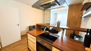 A compact kitchen with a built-in stove, a wooden countertop, a small sink, and a mirror above the counter. - Modern 1,5 - room apartment, Kadnárova 91 - Rača (Bratislava)