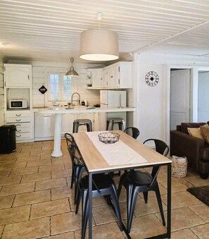A dining area with a table and chairs, a kitchen in the background, and a clock on the wall. - Vanille House with a Pool (Saint Pierre)