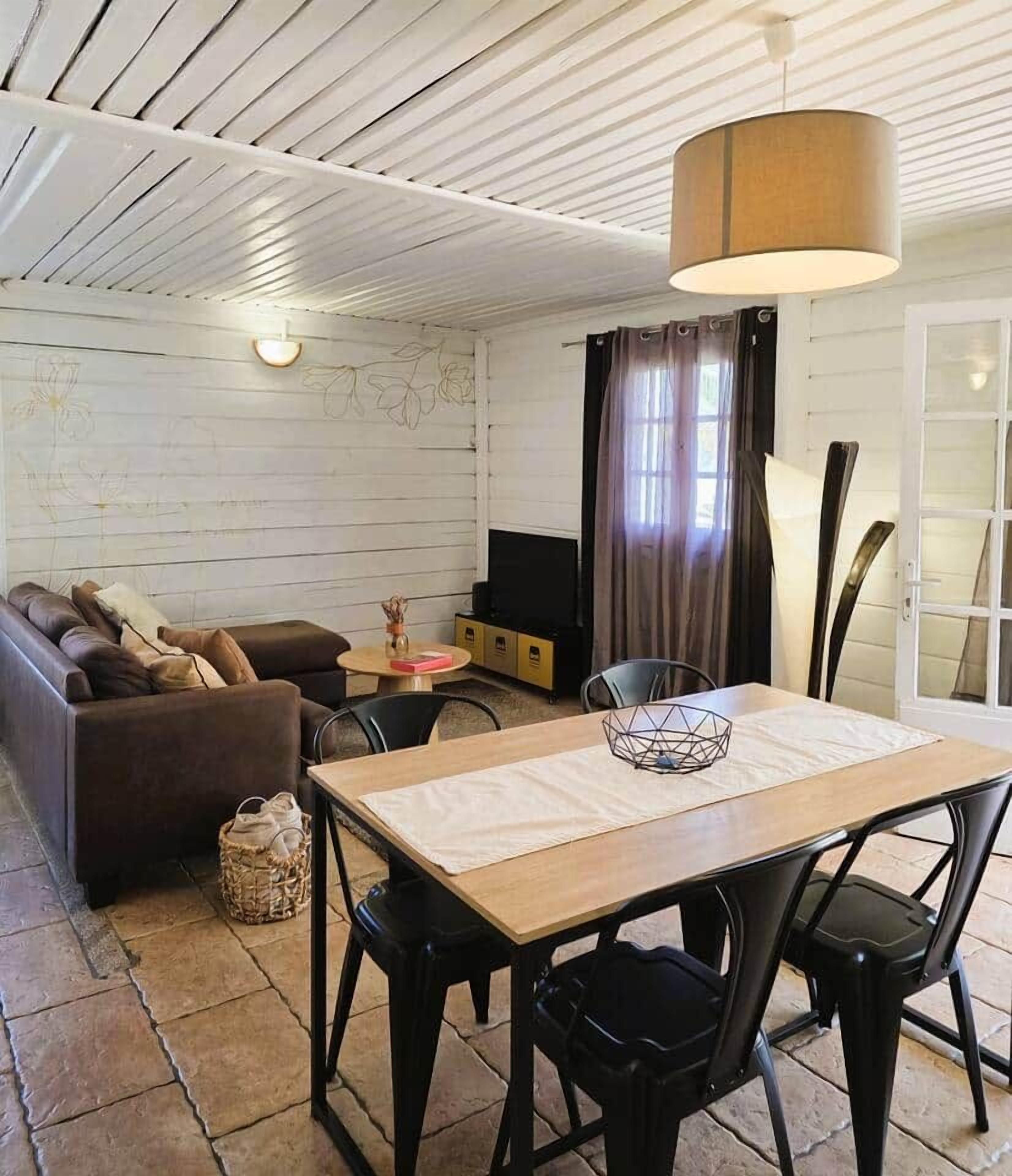 Una sala acogedora con sofá, mesa de comedor con sillas, lámpara y televisor.