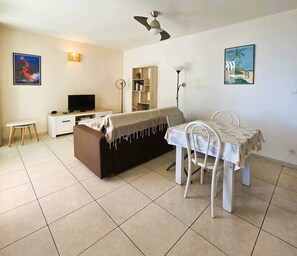 Quarto com cama, televisão, mesa de jantar com cadeiras, ventoinha no teto e obras de arte nas paredes.