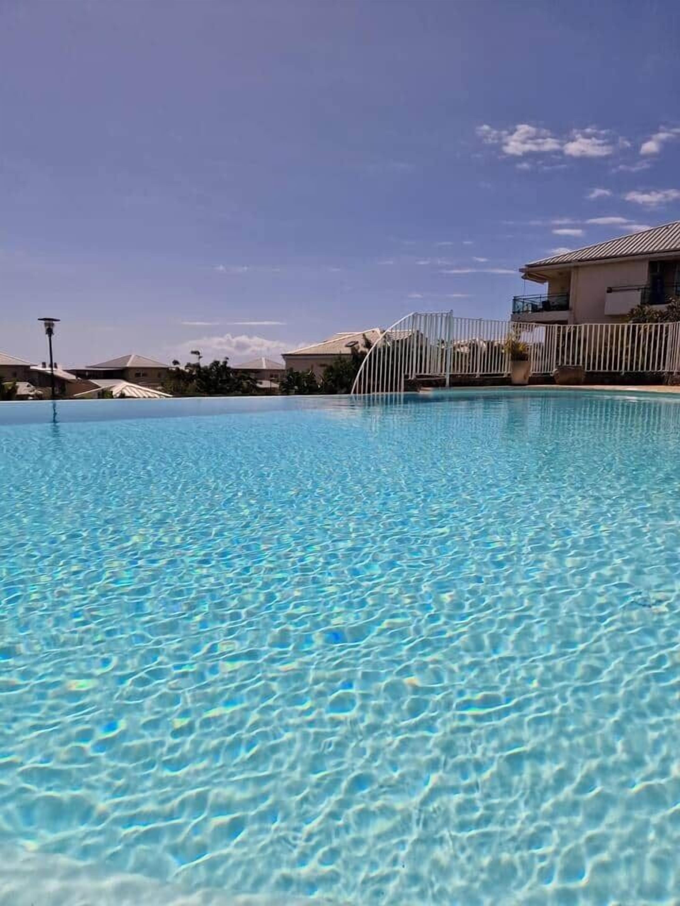 Uma piscina translúcida com grade e edifícios ao fundo.