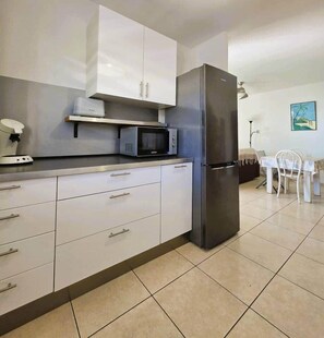 A modern kitchen with white cabinets, a stainless steel refrigerator, and a microwave. - *Loumava Apartment* (Saint-Paul)