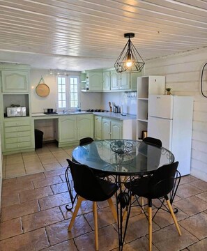 A kitchen with a round glass table and chairs, light green cabinets, and a hanging light fixture. - Vétiver House with a Pool (Saint Pierre)
