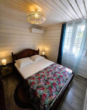 A single bed with a floral bedspread, a wooden headboard, bedside lamps, and a ceiling light fixture. - Vétiver House with a Pool (Saint Pierre)