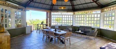Un patio cubierto con zona de comedor, mobiliario y vistas a la vegetación.