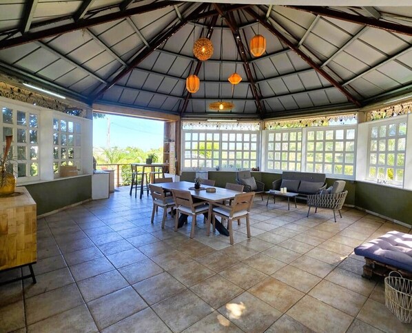 Une terrasse couverte comprenant un espace repas, des sièges et une vue sur la verdure environnante.