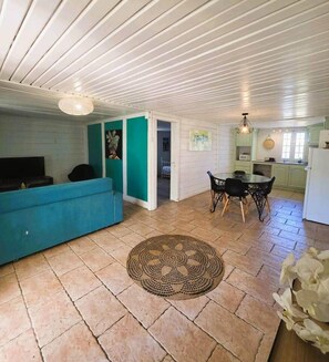 A living room with a sofa, a dining table with chairs, and a kitchen in the background. - Vétiver House with a Pool (Saint Pierre)
