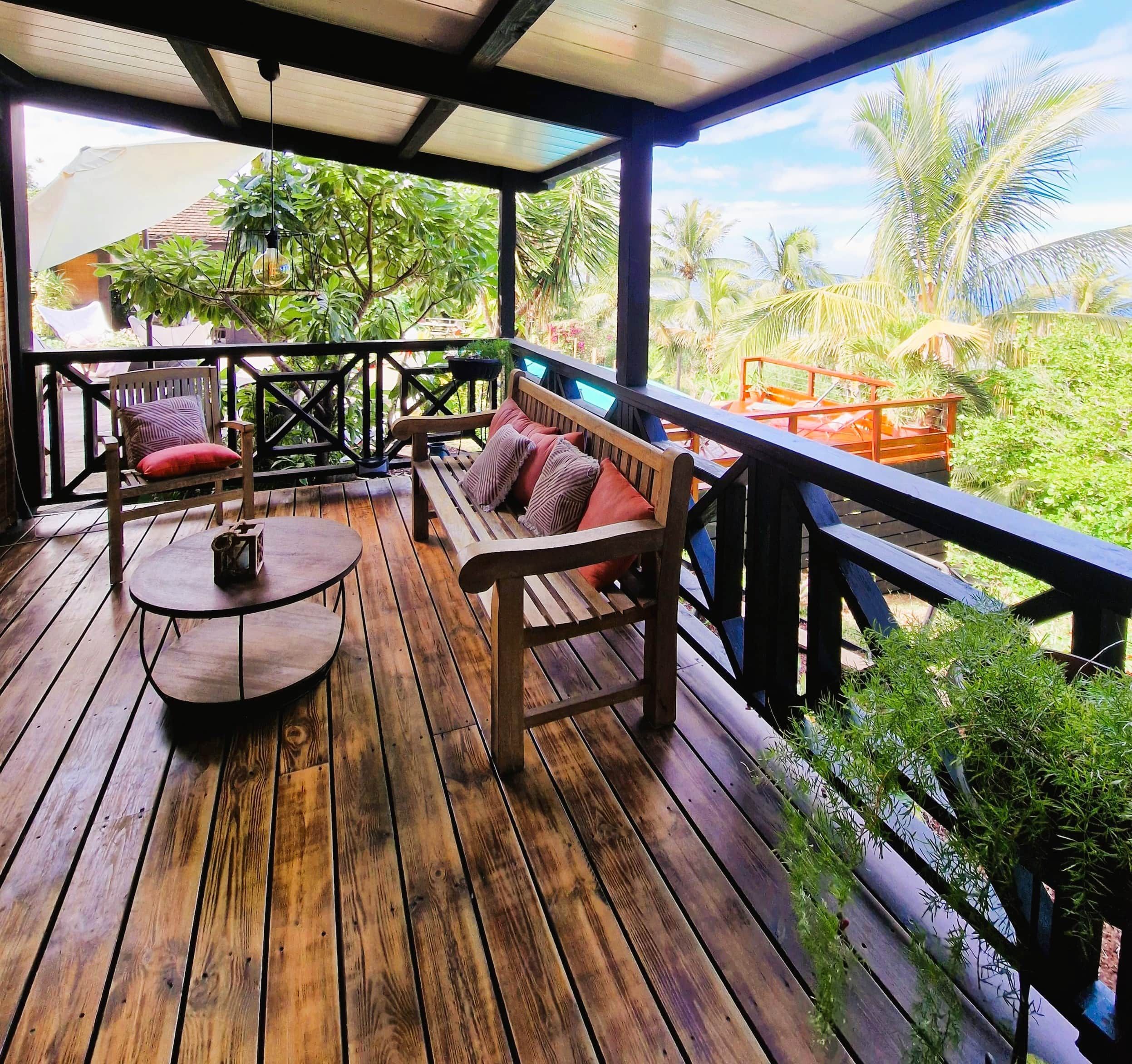 A wooden deck with a round table and two wooden benches with cushions.