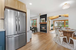 A modern kitchen with a stainless steel refrigerator, wooden cabinets, a fireplace, and a dining area with a table and chairs.
