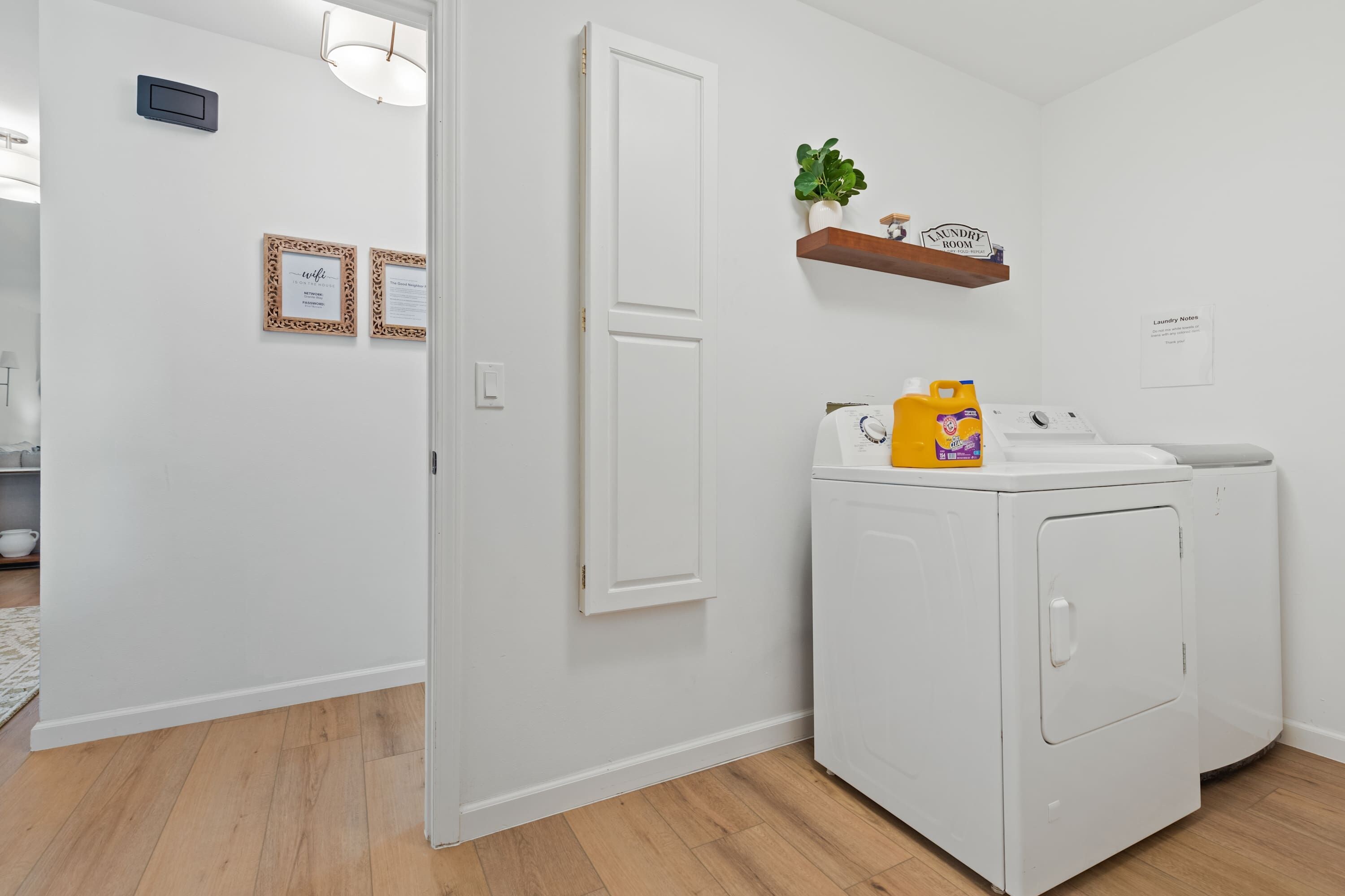 A laundry room with a washing machine, a dryer, and a shelf with a plant and a sign.