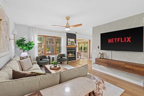 A modern living room with a large TV, a fireplace, and a ceiling fan.