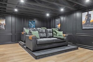 A dark-themed living room with a leather sofa, green cushions, and movie posters on the walls.