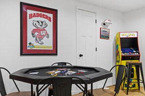 A room with a poker table, framed posters, a door, and a Pac-Man arcade machine.