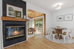 A modern living room with a fireplace, wooden ceiling, and a dining area with a round table and chairs.