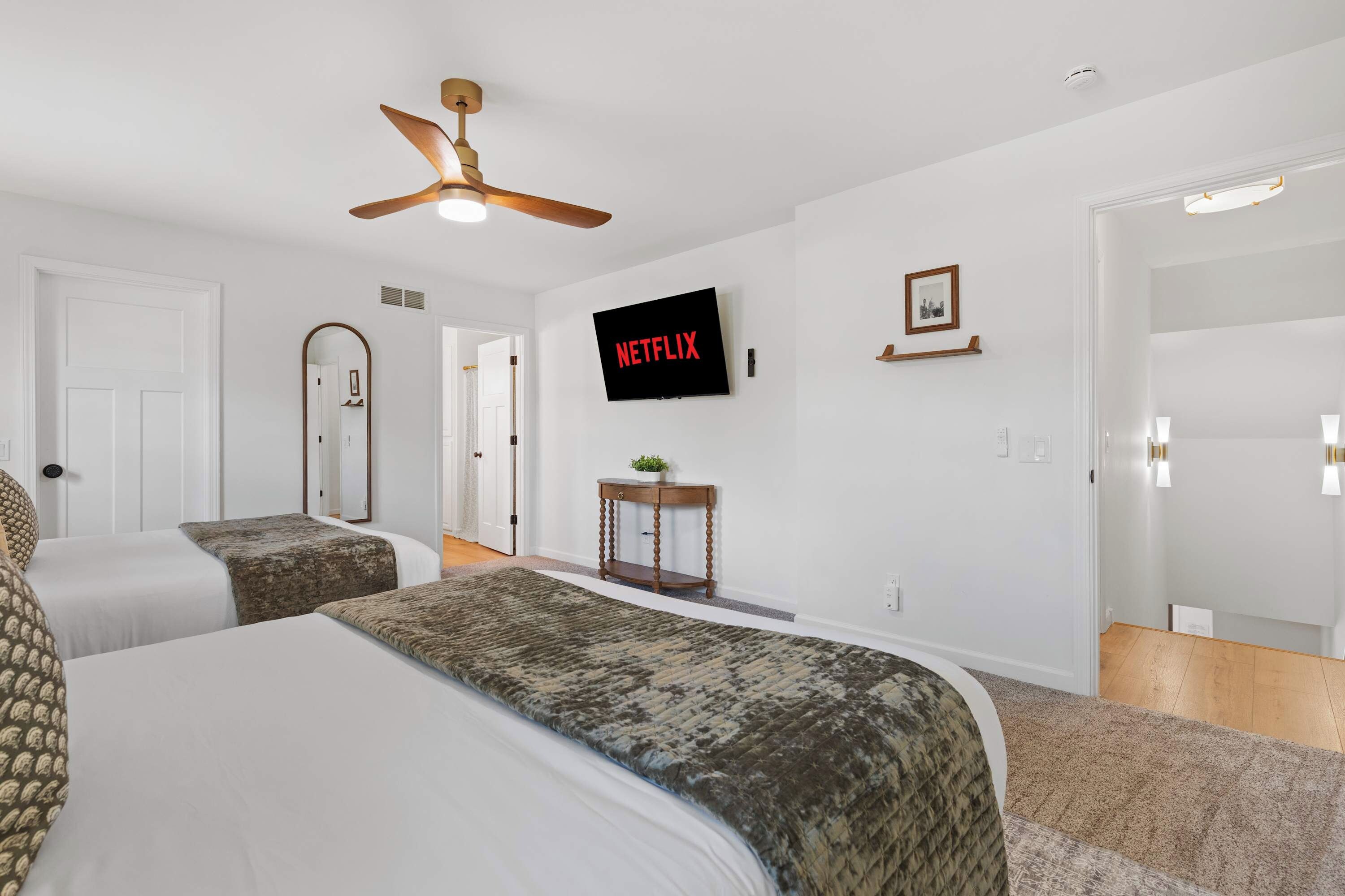 Une chambre d’hôtel avec deux lits, un ventilateur de plafond, un téléviseur fixé au mur et une porte donnant sur une autre pièce.