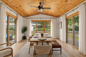 A dining area with a wooden ceiling, large windows, and a view of the outdoors.