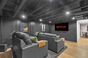 A modern home theater room with two leather recliners, a large flat-screen TV, and posters on the walls.