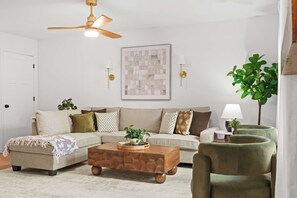 A living room with a sectional sofa, a wooden coffee table, a green armchair, a ceiling fan, and a wall-mounted lamp.
