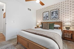 A bedroom with a wooden bed, two bedside tables with lamps, a ceiling fan, and patterned wallpaper.