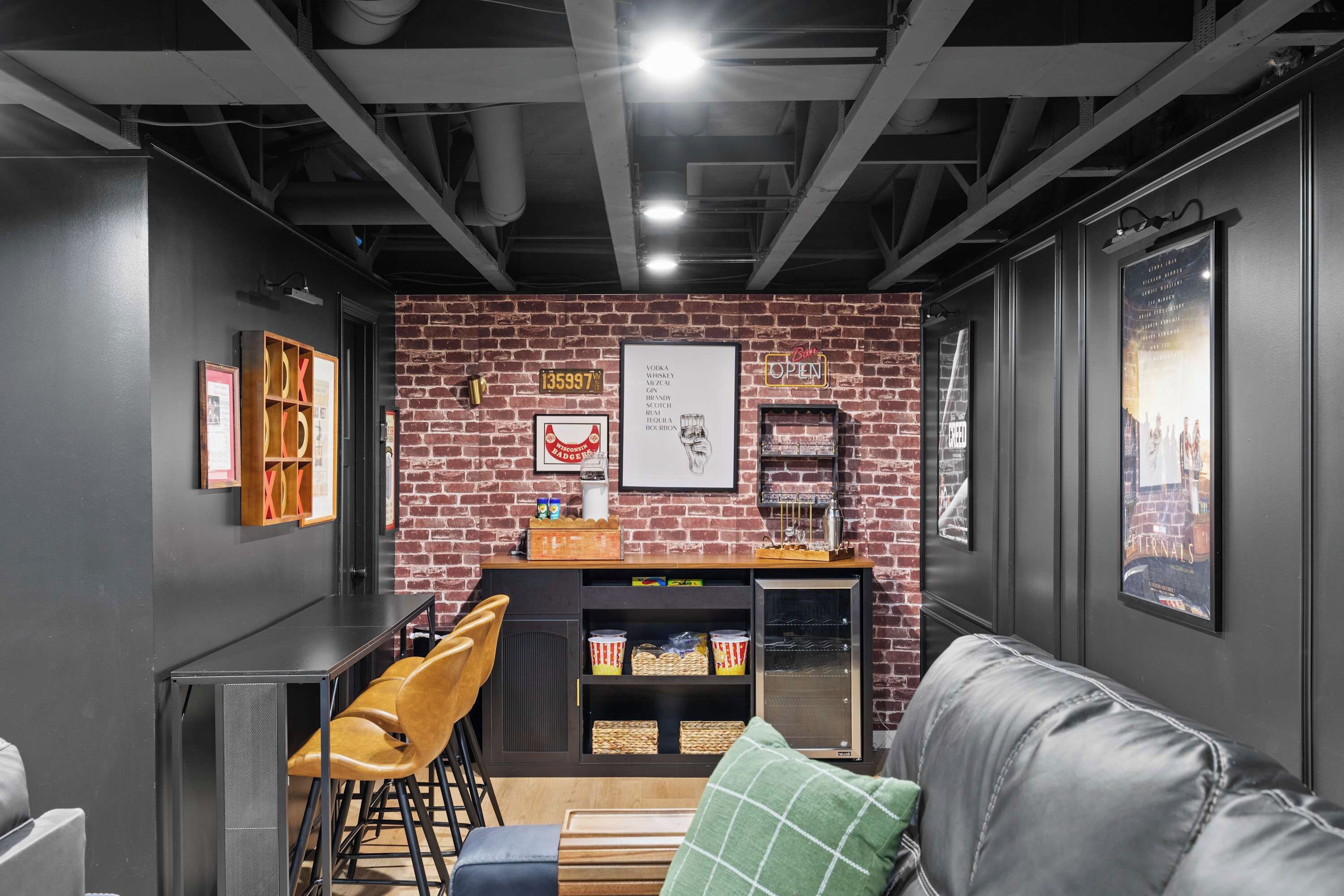 Un espace bar moderne avec un mur en briques, des tabourets de bar, un comptoir avec une caisse enregistreuse et un réfrigérateur rempli de boissons.