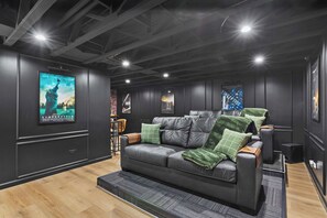 Ein modernes Wohnzimmer mit einem Ledersofa, grünen Kissen und einem Filmplakat an der Wand.