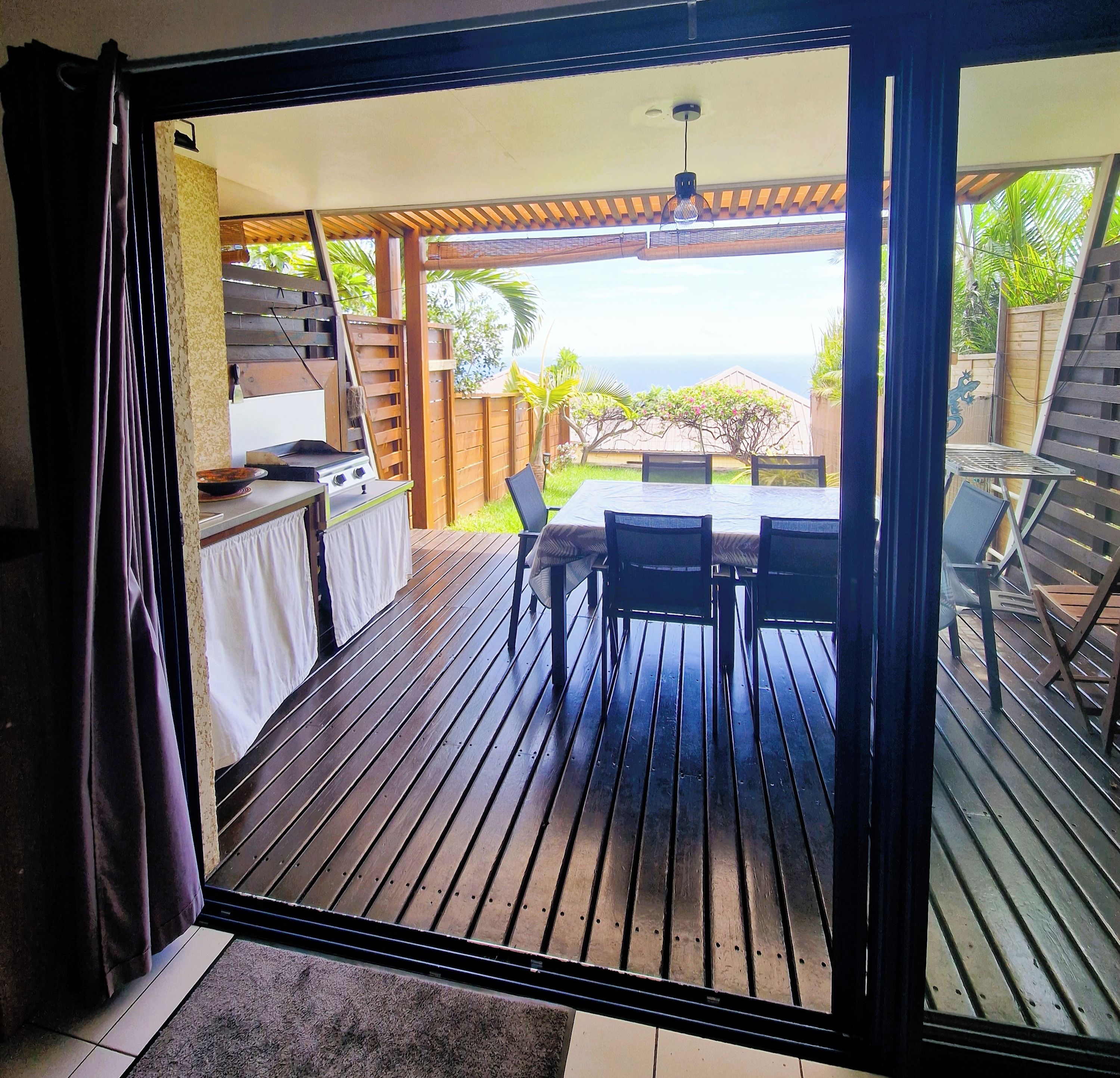An open sliding door leading to an outdoor patio with a grill, dining table, and chairs.
