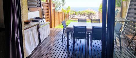 An open sliding door leading to an outdoor patio with a grill, dining table, and chairs.