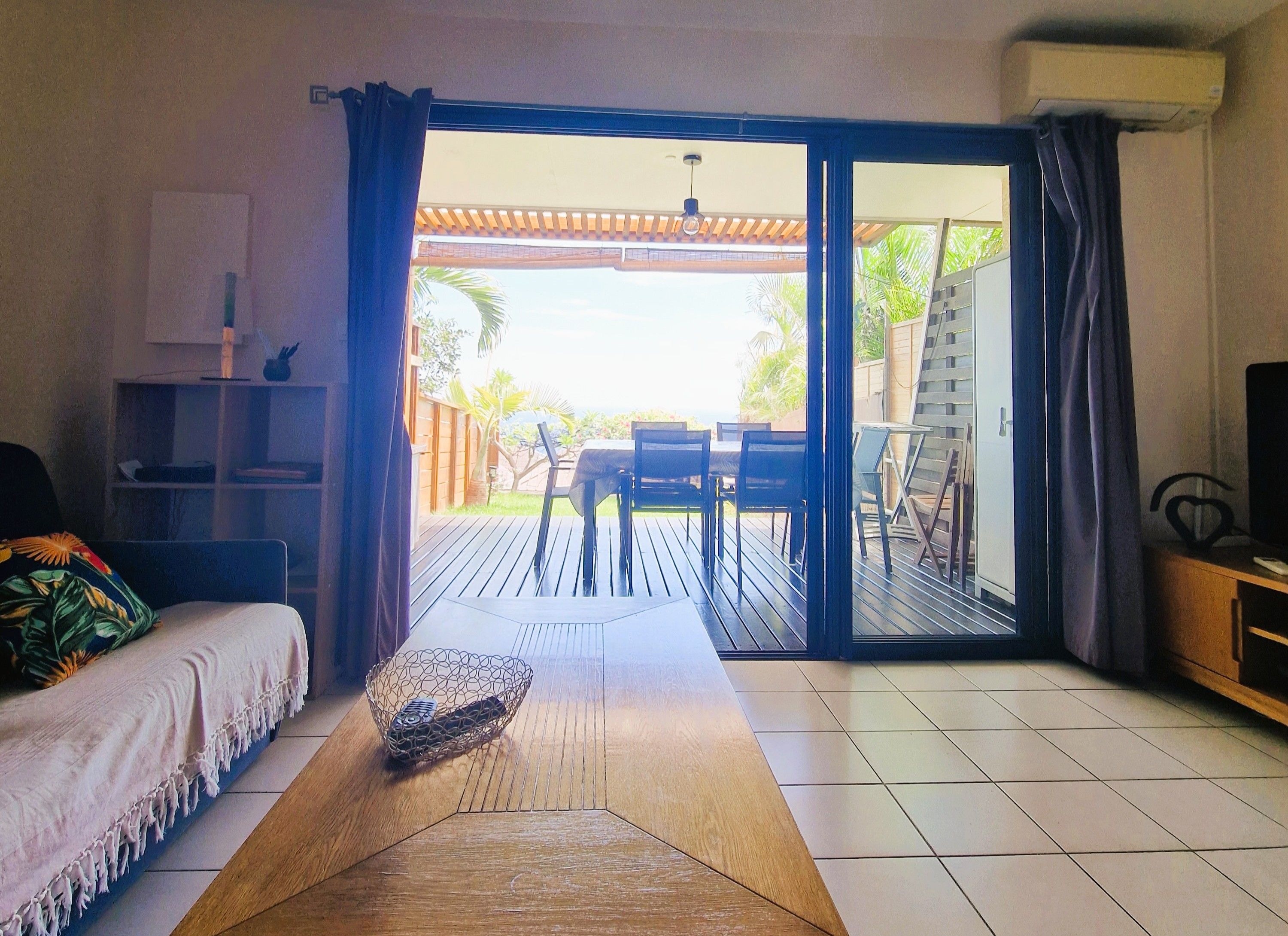 Et værelse med sofa, sofabord, fjernsyn og en skydedør til en udendørs patio med bord og stole.