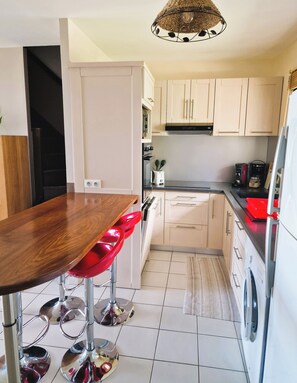 A modern kitchen with white cabinets, a wooden dining table, red bar stools, and a hanging light fixture. - Beautiful house in Piton-Saint-Leu, with a view of the sea (Saint-Leu)