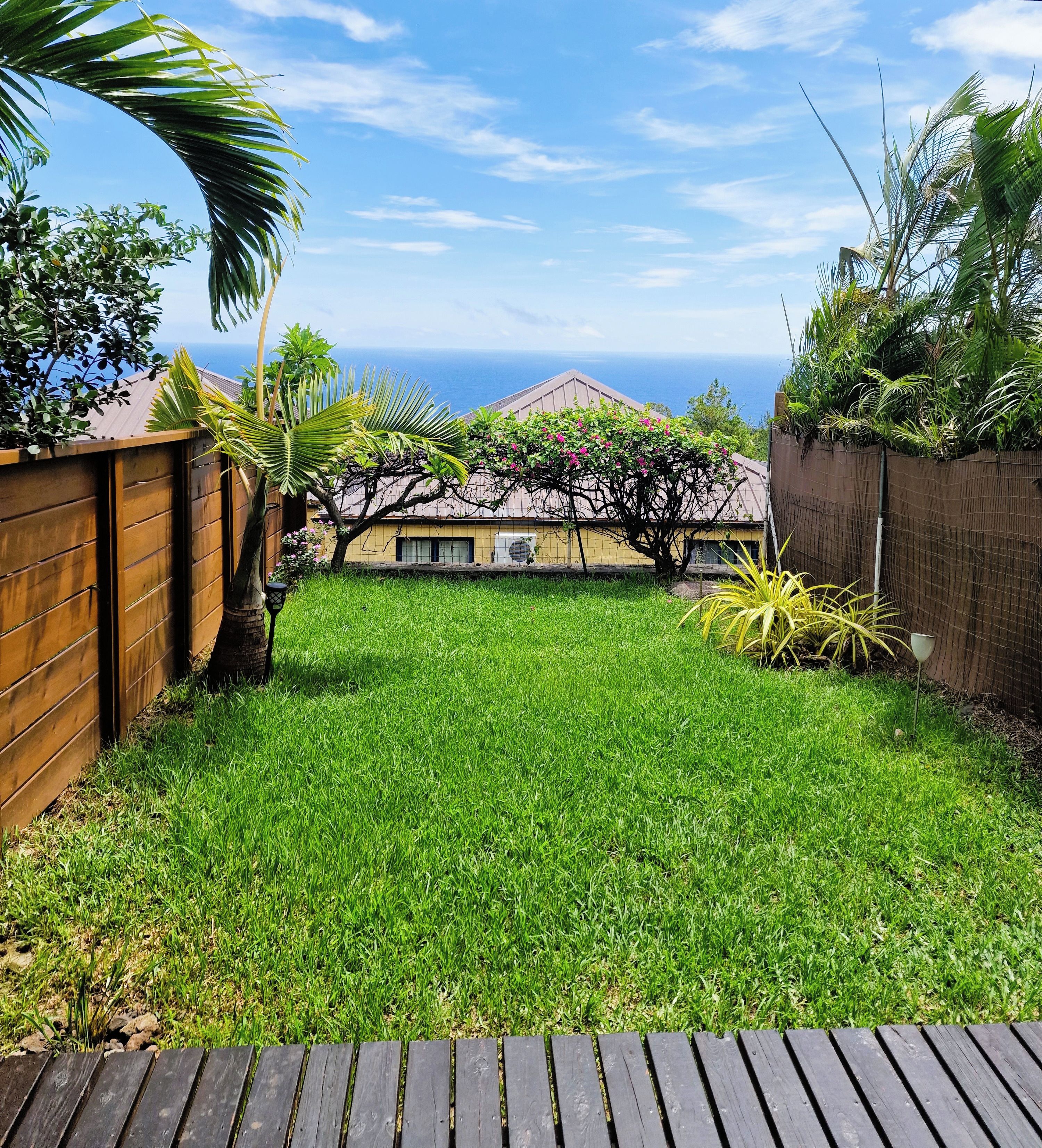 A backyard with a wooden deck, a grassy lawn, and a view of the ocean.