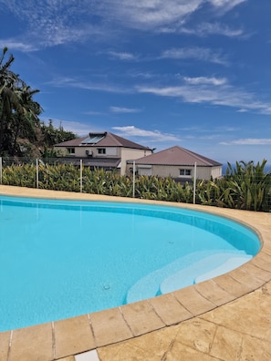 A swimming pool with a tiled edge, surrounded by a fence and greenery. - Beautiful house in Piton-Saint-Leu, with a view of the sea (Saint-Leu)