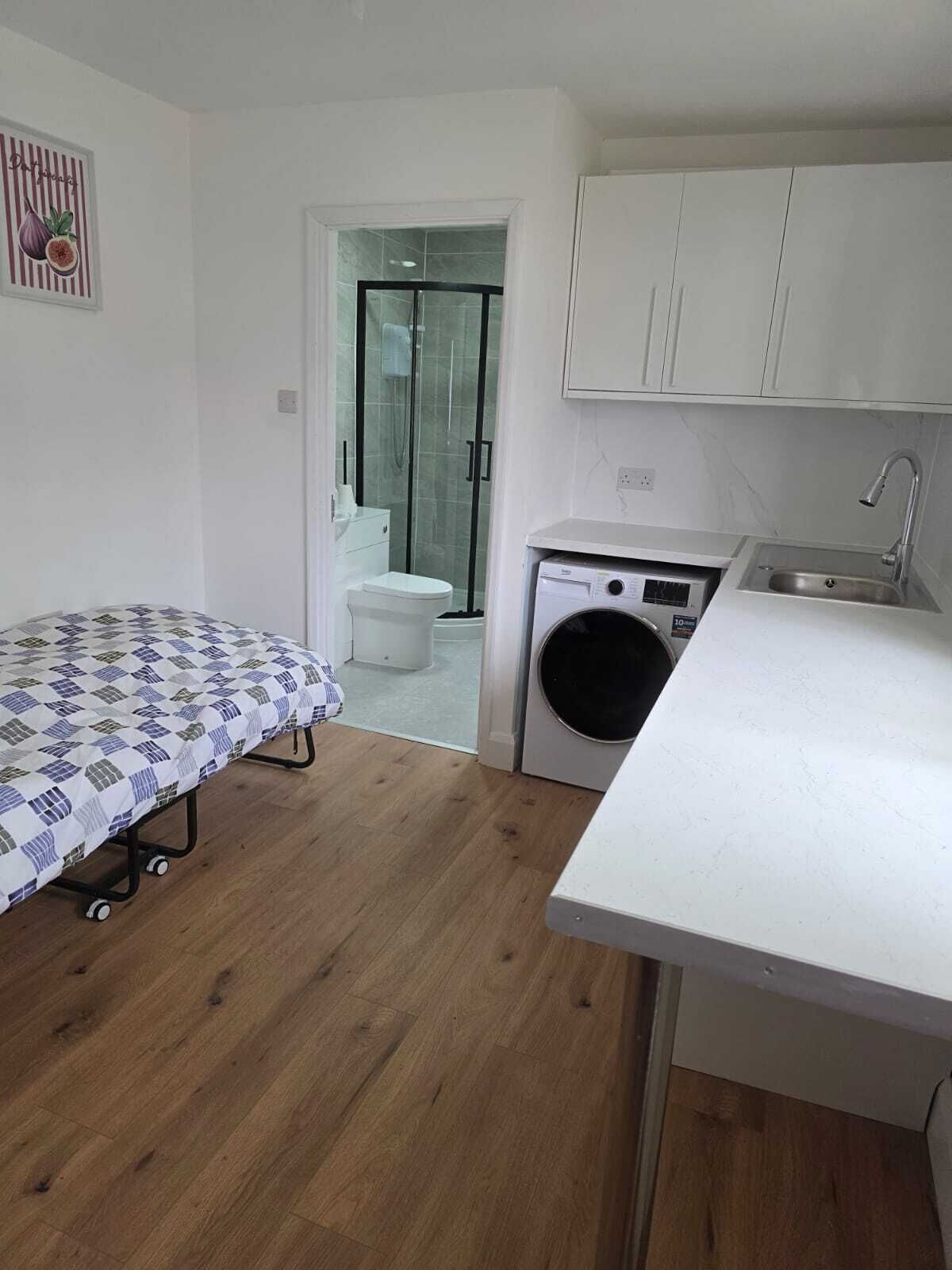 Une petite pièce comprenant un lit, un lave-linge, un évier et un espace douche.