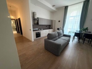 A modern apartment with a kitchenette, a grey sofa, and a dining area with a table and chairs. - NAPLES MARIANA LUXURY: SUPERIOR 2-BEDROOM APARTMENT IN THE CITY CENTER (Napoli)