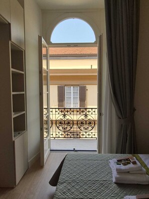 A bedroom with a bed, a wardrobe, a window with curtains, and a view of a balcony with a railing. - NAPLES MARIANA LUXURY: SUPERIOR 2-BEDROOM APARTMENT IN THE CITY CENTER (Napoli)