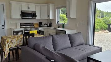 A compact living space with a kitchenette, a sofa, a dining table, and a view of the outdoors.