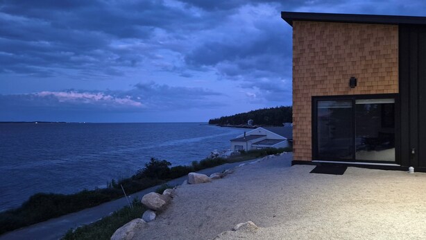A modern building with a brick facade and large glass doors, overlooking a body of water. - Brand-new oceanfront cottages with unobstructed views of the Atlantic Ocean. (Hubbards)