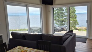 A room with a sofa, a dining table, and a view of a body of water through large sliding glass doors. - Brand-new oceanfront cottages with unobstructed views of the Atlantic Ocean. (Hubbards)