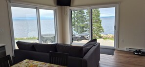 A room with a sofa, a dining table, and a view of a body of water through large sliding glass doors. - Brand-new oceanfront cottages with unobstructed views of the Atlantic Ocean. (Hubbards)