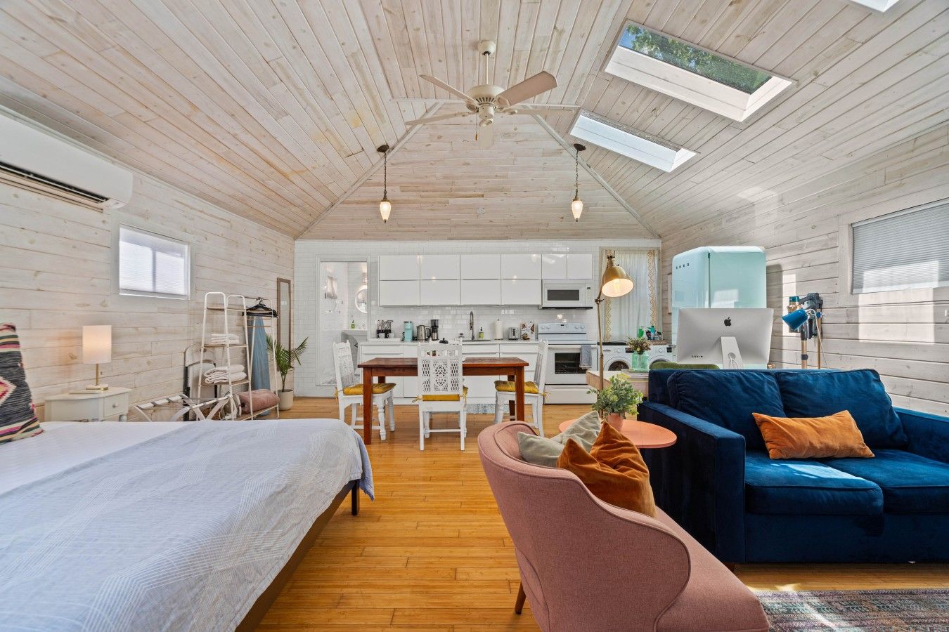 A modern interior with a bed, a blue sofa, a dining table, and a kitchen area.