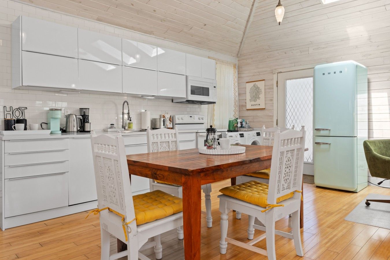 A modern kitchen with white cabinetry, a wooden dining table, and a vintage-style refrigerator.