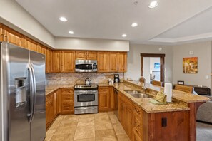 A modern kitchen with stainless steel appliances, wooden cabinets, and a granite countertop. - Crystal Peak Lodge by CoralTree Residences (Breckenridge)