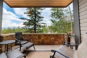 A covered patio area with stone walls, outdoor furniture, and a view of a tree and mountains. - Crystal Peak Lodge by CoralTree Residences (Breckenridge)