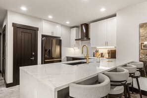 A modern kitchen with a marble countertop, stainless steel appliances, and a bar seating area. - Crystal Peak Lodge by CoralTree Residences (Breckenridge)