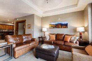A modern living room with leather sofas, a coffee table, and a dining area with wooden cabinets. - Crystal Peak Lodge (Breckenridge)