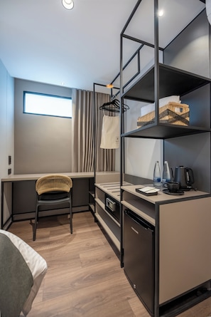 A compact hotel room with a bunk bed, a desk with a chair, a small kitchenette, and a window with curtains. - BLOSS HOTEL (Medellín)