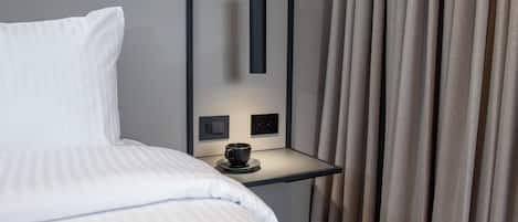 A hotel room with a bed, a bedside table with a cup, and curtains.