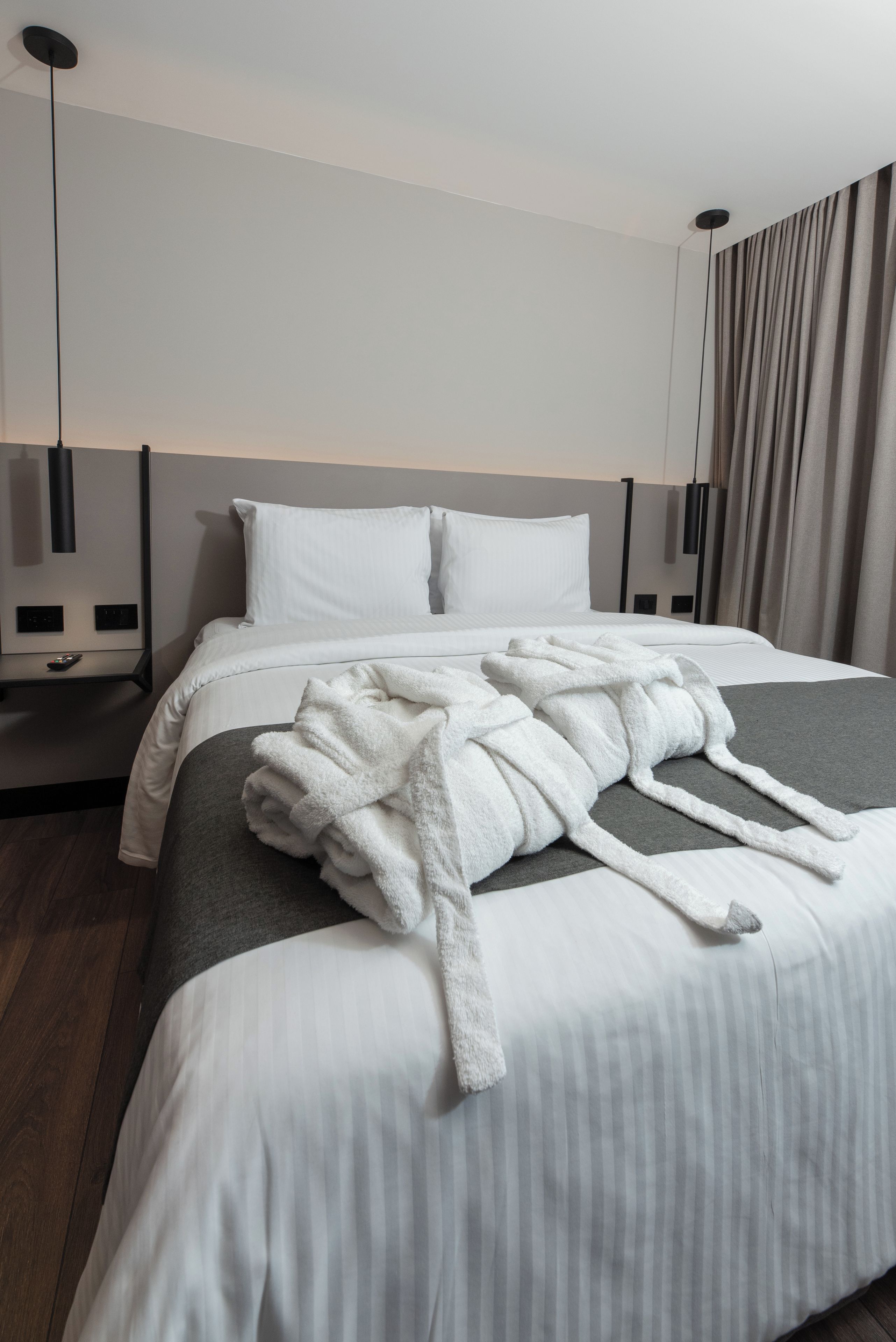 A hotel room with a neatly made bed, a remote control on the nightstand, and a modern light fixture.