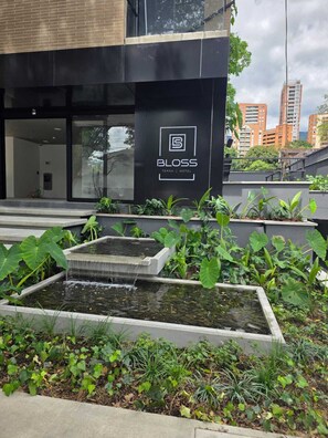 A modern hotel entrance with a water feature and lush greenery.
