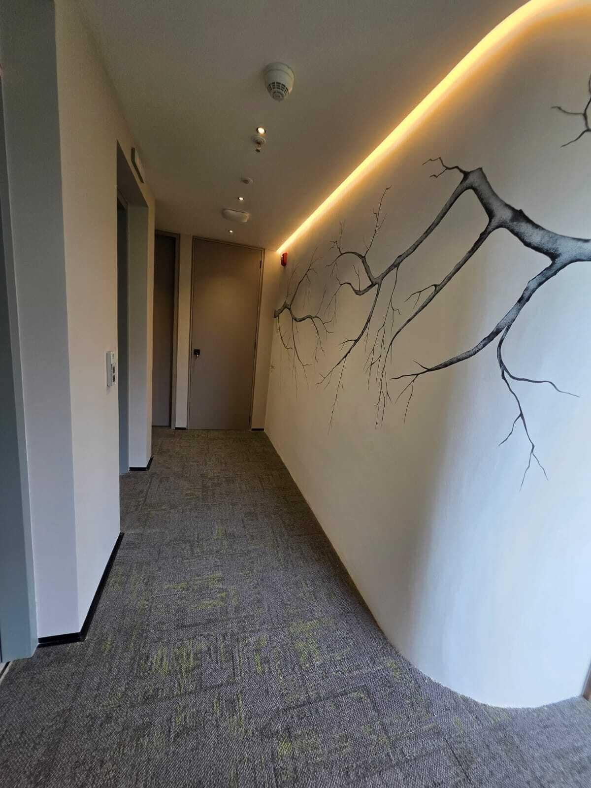 Un pasillo con alfombra texturizada, un cuadro de una rama de árbol en la pared, iluminación empotrada y una puerta al final.
